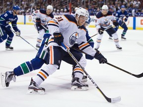 Edmonton Oilers' Drake Caggiula, front, skates towards the net with the puck while being checked by Vancouver Canucks' Ben Hutton during the third period of a preseason NHL hockey game in Vancouver, B.C., on Saturday September 30, 2017.
