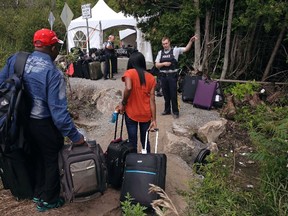 In this Aug. 7, 2017 file photo, a Royal Canadian Mounted Police officer informs a migrant couple of the location of a legal border station, shortly before they illegally crossed from Champlain, N.Y., to Saint-Bernard-de-Lacolle, Quebec, using Roxham Road. (Charles Krupa/The Canadian Press/AP)