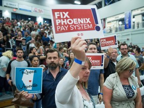 Federal government workers hold up signs about the Phoenix pay system as Prime Minister Justin Trudeau leaves after a town hall at Kelowna, B.C., on Sept. 6.