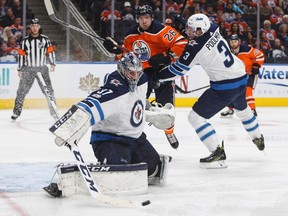 Jets goalie Connor Hellebuyck makes a save as defenceman Tucker Poolman battles with the Oilers’ Iiro Pakarinen last night in Edmonton. (The Canadian Press)