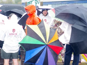 Striking workers at Cami huddled together during a rain deluge Wednesday morning in Ingersoll. (HEATHER RIVERS, Woodstock-Sentinel Review)