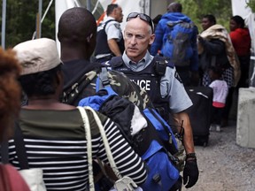An RCMP officer standing in Saint-Bernard-de-Lacolle, Que., advises migrants that they are about to illegally cross from Champlain, N.Y., and will be arrested, on Aug. 7, 2017. A spokesman for Public Safety Minister Ralph Goodale says an RCMP questionnaire that singled out Muslim asylum seekers has been deemed inappropriate and taken out of circulation. (Charles Krupa/AP Photo/Files)