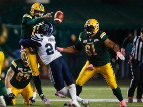 Toronto Argonauts' Justin Tuggle, centre, forces Edmonton Eskimos quarterback Mike Reilly to ditch the ball during second half CFL football action in Edmonton, Saturday, Oct. 14, 2017. THE CANADIAN PRESS/Jeff McIntosh