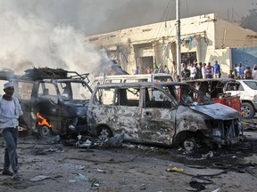 Somalis walk past the wreckage of vehicles at the scene of a blast in the capital Mogadishu, Somalia Saturday, Oct. 14, 2017. A huge explosion from a truck bomb has killed at least 20 people in Somalia's capital, police said Saturday, as shaken residents called it the most powerful blast they'd heard in years. (AP Photo/Farah Abdi Warsameh)