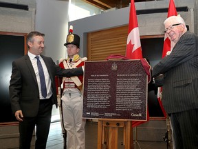 Jonathan Moore, left, an archeologist for Parks Canada and Richard Alway, chair of Historic Sites and Monuments Board of Canada unveil a plaque marking Kingston shipwrecks from the War of 1812 as a national historic site. Standing guard is a Canadian Fencibles military re-enactor at the Fort Henry Discovery Centre in Kingston. (Ian MacAlpine /The Whig-Standard)