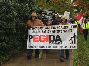 Pegida Canada members Gayle Cooper, left, and Dave Capuano march down Dufferin Avenue to Victoria Park holding the group's banner Saturday morning. The city hall rally by the anti-Islamist group was met with dozens of anti-hate protesters, who banged drums, pots and pans to drown out their message. (Jennifer Bieman/The London Free Press)