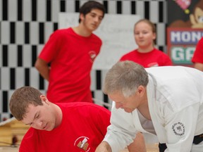 Master Instructor Hanshi Ken Tallack shows a student how to finish breaking six boards with his hand during the 2015 Break-A-Thon fundraiser held at the Frontenac Mall in Kingston, Ont. on Saturday July 11, 2015. Tallack is being inducted into the Canadian Black Belt Hall of Fame this weekend.  
Julia McKay/The Kingston Whig-Standard/Postmedia Network