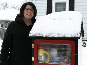 Brianne Kortum poses by the Bean's Books "free little library" in front of her Capel Street home. For December, it's been converted into a "free little pantry" for food and hygiene items.  Tyler Kula/Sarnia Observer/Postmedia Network