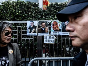 Former Hong Kong lawmaker Leung Kwok-hung (L) -- known as "Long Hair" -- stands next to posters of (back L to R) Chinese dissident Huang Qi, human rights lawyer Xie Yang, jailed Chinese activist Wu Gan, known by the online pseudonym "Super Vulgar Butcher" and democracy activist Qin Yongmin, as a policeman (front R) walks past during a protest outside the Chinese Liaison Office in Hong Kong on December 27, 2017.
A court in mainland China on December 26 sentenced Wu Gan to eight years in prison after he refused to plead guilty to charges of "subverting state power".  / AFP PHOTO / Anthony WALLACEANTHONY