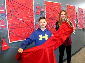 Grade 9 John McGregor Secondary School students Riley Gray (left) and Kacey Day are among the students in Jennifer McQuade's art class who are taking part in the Red Dress Project that brings awareness to missing and murdered Indigenous women and girls in Canada. They are shown in front of an art installation representing a broken web to resemble a dream catcher located in the library and holding one of the many red dresses that hang inside and outside the school in Chatham. Ellwood Shreve/Postmedia Network