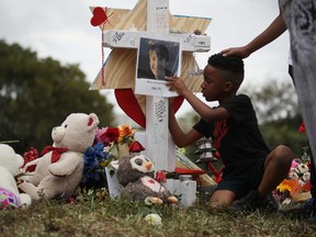 Nekhi Charlemagne writes a message on a cross setup in a makeshift memorial in front of Marjory Stoneman Douglas High School on February 19, 2018 in Parkland, Florida. (Joe Raedle/Getty Images)