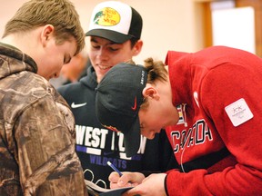 Canadian Paralympic sledge hockey athlete James Dunn, right, signs an autograph for West Elgin Secondary School Grade 9 students Owen Lunn and Matthew Zinkan. Tom Morrison/Postmedia News