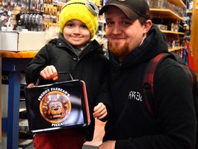 Rowen Thompson, left, holds his lunchbox beside father Matthew Thompson inside Fan of the Sport Thursday morning. The store will be one of many giving away free comic books May 5 and participating in the new Superhero Saturday -- a community-wide event for all things superhero. (Louis Pin/Times-Journal)