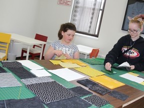 Hailey Stewart (left) and Payton Brady carefully select the colour pattern they will sew into a square for a Humboldt Broncos comfort quilt.
