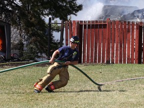 A firefighter pulls a hose along a backyard while trying to put out a fire in a shed on Monday.