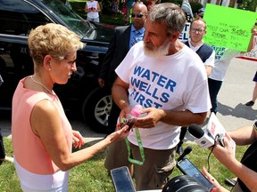 Premier Kathleen Wynne is shown a sample of black water taken from a local water well by Water Wells First spokesperson Kevin Jakubec during a stop in Chatham, Ont. on Thursday July 27, 2017. The citizen group has received commitments from four other political parties, including the Progressive Conservatives, the New Democrats, the Green Party and the Trillium Party, that a health hazard investigation will be conducted on affected wells in the North Kent Wind project area if they are elected as the government in the upcoming provincial election on June 7, 2018. (Ellwood Shreve/Chatham Daily News)