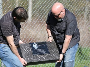 Jeff Holtz, left, and Dave Mills hold a monument to Garrett Mills that they placed near the fence bordering a park on King Street in Napanee on Saturday, one year after Garrett’s death. (Meghan Balogh/The Whig-Standard/Postmedia Network)