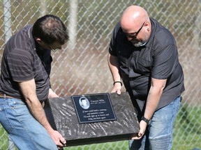 Meghan Balogh/postmedia network
Jeff Holtz, left, and Dave Mills hold a monument to Garrett Mills that they placed near the fence bordering a park on King Street in Napanee on Saturday, one year after Garrett’s death.