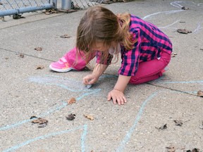 A child colours in her chalk outline in front of a daycare.