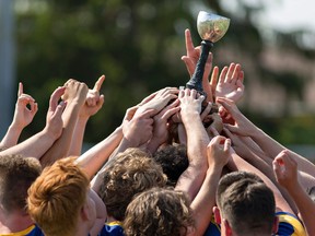 Members of the BCI senior boys rugby team reach to touch the trophy after defeating St. John's College to claim the Brant County high schools senior boys rugby championship on Thursday in Brantford. (Brian Thompson/The Expositor)