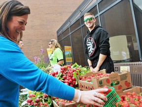 Jenn Scherle takes a crate of strawberries from the Sarah's Farm Market table at a farmers’ market held Monday at the Chatham-Kent Civic Centre as Mitchell Benn looks on. The market was organized to kick off Local Food Week, which runs until June 10. Tom Morrison/Chatham This Week