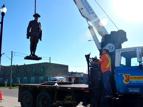 Tim Russell, left, hoists the Great War memorial statue onto a skid Monday morning. The memorial will be refurbished this week, one of the final touches to the $280,000 memorial garden project on Moore Street. (Louis Pin/Times-Journal)