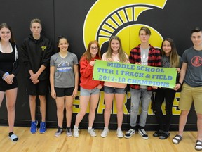 Sophie Ferguson (from left to right), Grady Hauk, Abygale Reeve, Hailey McAvena, Amanda Paquette, Owen Fitchett, Hunter Aman, and Cody Jaman stand side by side presenting a banner labelling them as champions. The track and field athletes did exceptional in this year's South-Central zone competition.