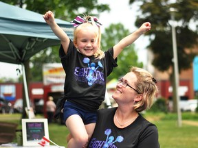 Amie Bell, right, holds up her daughter Kerrigan outside the Eight Count Cheer Academy tent at Tecumseh Park during CK Summer Fest Saturday. (Tom Morrison/Postmedia Network)