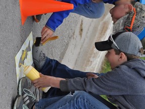 Grade 4 students painting yellow fish beside drains in Goderich to educate and remind people that what goes down these drains, eventually ends up in Lake Huron and affects the fish and other living creatures. Pictured here: Max Kraft and Hudson Ireland. (Contributed photo)