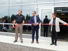 Robert Edmonds, from Drive Products, cuts the ribbon Friday afternoon at the grand opening of the newly expanded Voth Truck Bodies manufacturing facility in Courtland. Holding the ribbon are Frank Voth, president of Voth Truck Bodies, left, and Greg Edmonds, founder of Drive Products. The distribution and manufacturing companies merged about three years ago, but the Courtland manufacturing company still operates as Voth Truck Bodies. (Chris Abbott/Postmedia Network)