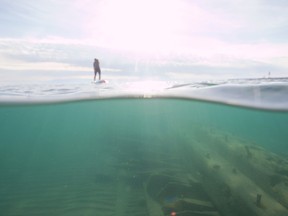West Shore Clothing owner Ash Adams is seen paddleboarding over Lake Huron's waves, while below, the wreck of the schooner Ann Maria is seen on the lake bottom near the south pier at Kincardine's Station Beach in summer 2018. (Shared photo by Ryan Osman)