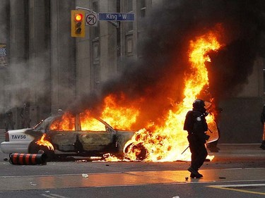 Riot police pass a cruiser is set ablaze by anti-G20 protesters in Toronto, June 26, 2010. Craig Robertson/QMI Agency