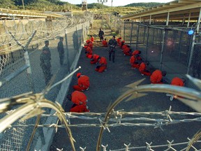 Detainees in orange jumpsuits sit in a holding area under the watchful eyes of military police during in-processing to the temporary detention facility at Camp X-Ray of Naval Base Guantanamo Bay in this January 11, 2002 file photograph.   (REUTERS)