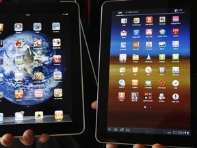 An employee of South Korean mobile carrier KT holds a Samsung Electronics’ Galaxy Tab 10.1 tablet (R) and Apple Inc’s iPad tablet as he poses for photos at a registration desk at KT’s headquarters in Seoul August 10, 2011.  REUTERS/Jo Yong-Hak