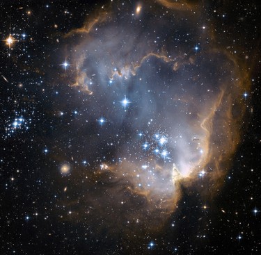 This photo from the Hubble Space Telescope, supplied by NASA and the European Space Agency on Monday, Jan 8, 2007, shows bright blue newly formed stars that are blowing a cavity in the centre of a star-forming region known as N90 that has fascinated scientists. The high energy radiation blazing out from the hot young stars in N90 is eroding the outer portions of the nebula from the inside, as the diffuse outer reaches of the nebula prevent the energetic outflows from streaming away from the cluster directly. Because N90 is located far from the central body of the Small Magellanic Cloud, numerous background galaxies in this picture can be seen, delivering a grand backdrop for the stellar newcomers. The dust in the region gives these distant galaxies a reddish-brown tint. (NASA/ESA)