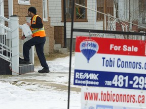 A postal worker runs through his route near a for sale sign posted at a house in the Westmount neighbourhood of Edmonton, Alberta, in a file photo. (IAN KUCERAK/EDMONTON SUN FILE)