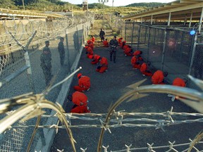 Detainees in orange jumpsuits sit in a holding area under the watchful eyes of military police during in-processing to the temporary detention facility at Camp X-Ray of Naval Base Guantanamo Bay in this January 11, 2002 file photograph. (REUTERS/Stringer/Files)