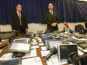 Det.-Const. Dave Forbes, right, stands before all the stolen items recently recovered after Toronto Police busted up a car robbery theft ring between Jan. 26-28 arresting four suspects. Some of the over 200 items ranged from GPS devices, cellphones, designer sunglasses, car stereos, passports, tool kits, laptops wallets and even a priests Mass and Last Rites kit — which officers said was stolen in 2007. (JACK BOLAND/Toronto Sun)