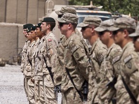 Canadian (left, in focus) and American (right, out of focus) military personnel stand at attention during the transfer of authority ceremony of the Ma'sum Ghar forward operating base (FOB) and the Panjwa'i district, in the Ma'sum Ghar FOB in the province of Kandahar, in Afghanistan, on July 5 2011. (PHILIPPE-OLIVIER CONTANT/QMI Agency)