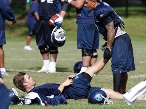 Mike Bradwell gets his leg stretched by Chad Owens at the end of practice Wednesday. After several days of intense workouts, the Argos were rewarded by being sent home early. (MICHAEL PEAKE/Toronto Sun)