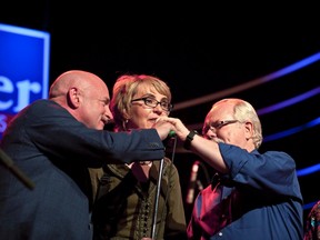 Retired astronaut Mark Kelly, husband of former U.S. congresswoman Gabrielle Giffords, and her former aide Democrat Ron Barber, who is running for her previous post, both help to adjust Giffords' microphone as she speaks onstage in support of Barber, at his "Get Out the Vote Concert and Rally" election campaign event at the Rialto Theatre in Tucson, Arizona June 9, 2012. (REUTERS/Samantha Sais)