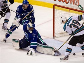Vancouver Canucks goalie Roberto Luongo, center, stops San Jose Sharks' Logan Couture as Canucks' Chris Tanev looks on during the third period of an NHL hockey game in Vancouver, British Columbia, Saturday, Jan. 21, 2012. The Canucks won 4-3. (AP Photo/The Canadian Press, Darryl Dyck)