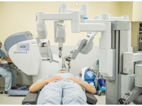 Dr. Eitan Prisman sits at the da Vinci surgical robot while his former patient, Igor Zaporozhets lies on the operating room table like he did when the robot assisted with his cancer removal operation.