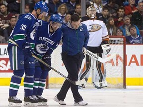 Vancouver Canucks blue-liner Dan Hamhuis (centre) is helped off the ice by teammate Henrik Sedin (left) and one of the team’s trainers after tearing his groin during a Nov. 20, 2014 NHL game against the Anaheim Ducks at Rogers Arena. (Darryl Dyck, Canadian Press)