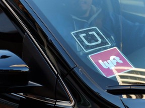 A driver displaying Lyft and Uber stickers on his front windshield drops off a passenger in downtown Los Angeles, Calif. Passengers arriving at Los Angeles International Airport will be allowed to leave in an UberX car starting Thursday, Jan. 21.