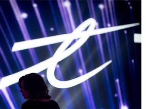 A woman is silhouetted as the Telus Corp. logo is displayed on a screen during a company event in Vancouver, B.C., on Friday, October 2, 2015. Telus Corp. says it's planning to reduce its workforce by 1,500 positions in an effort to cut annual costs by up to $125 million.