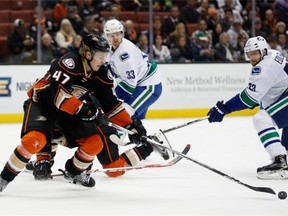 Hampus Lindholm #47 of the Anaheim Ducks reaches for the puck as Alexander Edler #23 and Henrik Sedin #33 of the Vancouver Canucks follow the play during the second period of a game at Honda Center on November 30, 2015 in Anaheim, California.