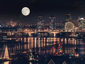 File: A full moon and city lights provide a dramatic backdrop as a parade of Christmas Carol Ships sets out for an evening cruise in the marine community of False Creek.