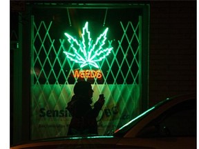 A pedestrian walks past the Weeds neon sign at the store front for medical marijuana dispensary in Vancouver.