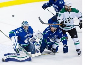 A shot deflects off the shoulder of Vancouver Canucks’ goalie Ryan Miller, left, as Chris Tanev (8) defends against Dallas Stars’ Patrick Eaves, right, during the second period of an NHL hockey game in Vancouver, B.C., on Thursday December 3, 2015.